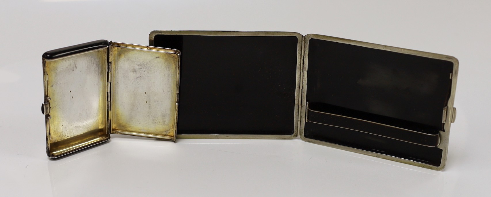 A French Art Deco white metal, black lacquer and eggshell banded cigarette case, with cabochon button, 8cm and one other similar larger cigarette case though apparently unmarked.